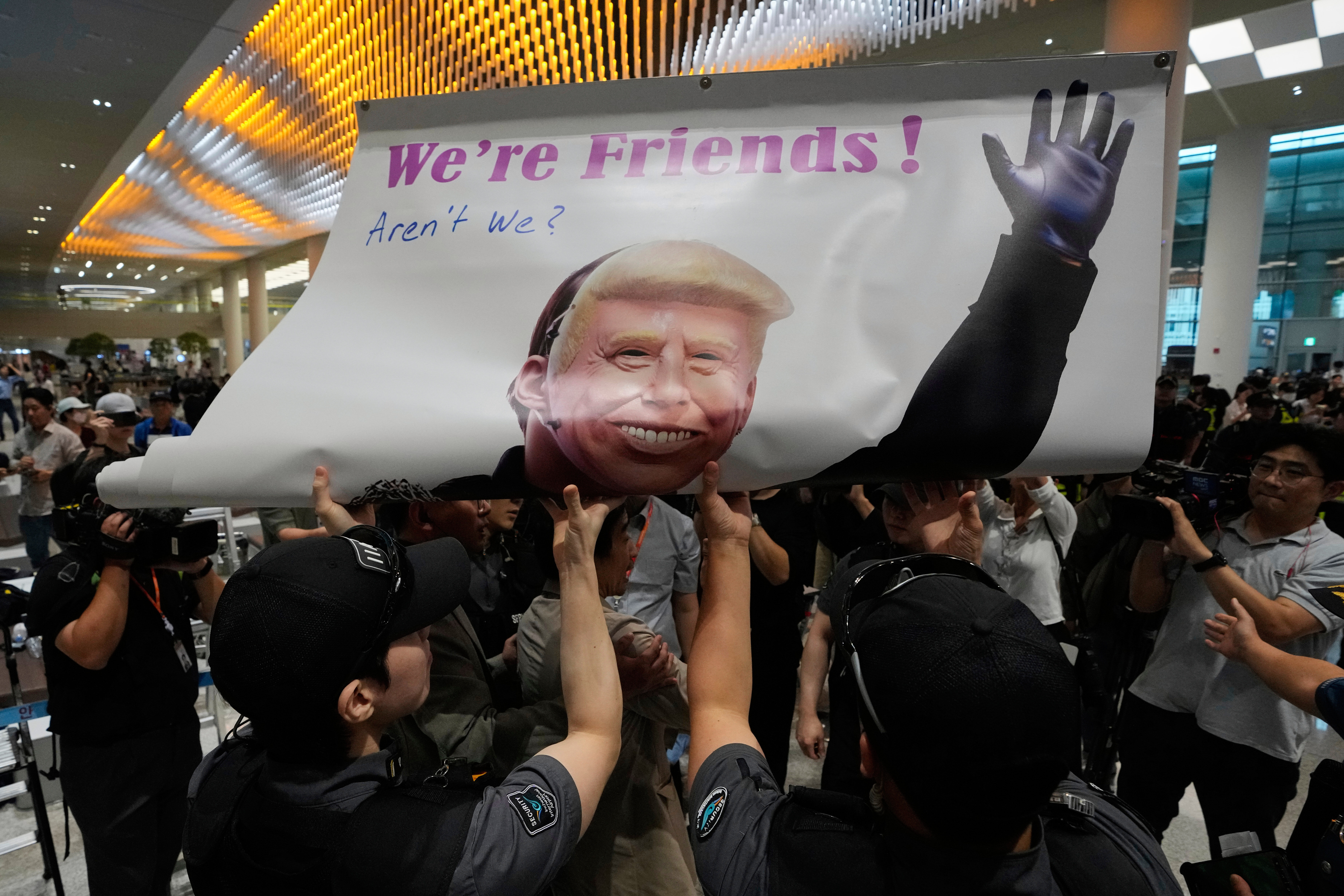 Protesters try to hold a banner depicting U.S. President Donald Trump as police officers and members of airport security block at the arrival terminal of the Incheon International Airport, in Incheon, South Korea, Friday, Sept. 12, 2025. (Ahn Young-joon - AP)