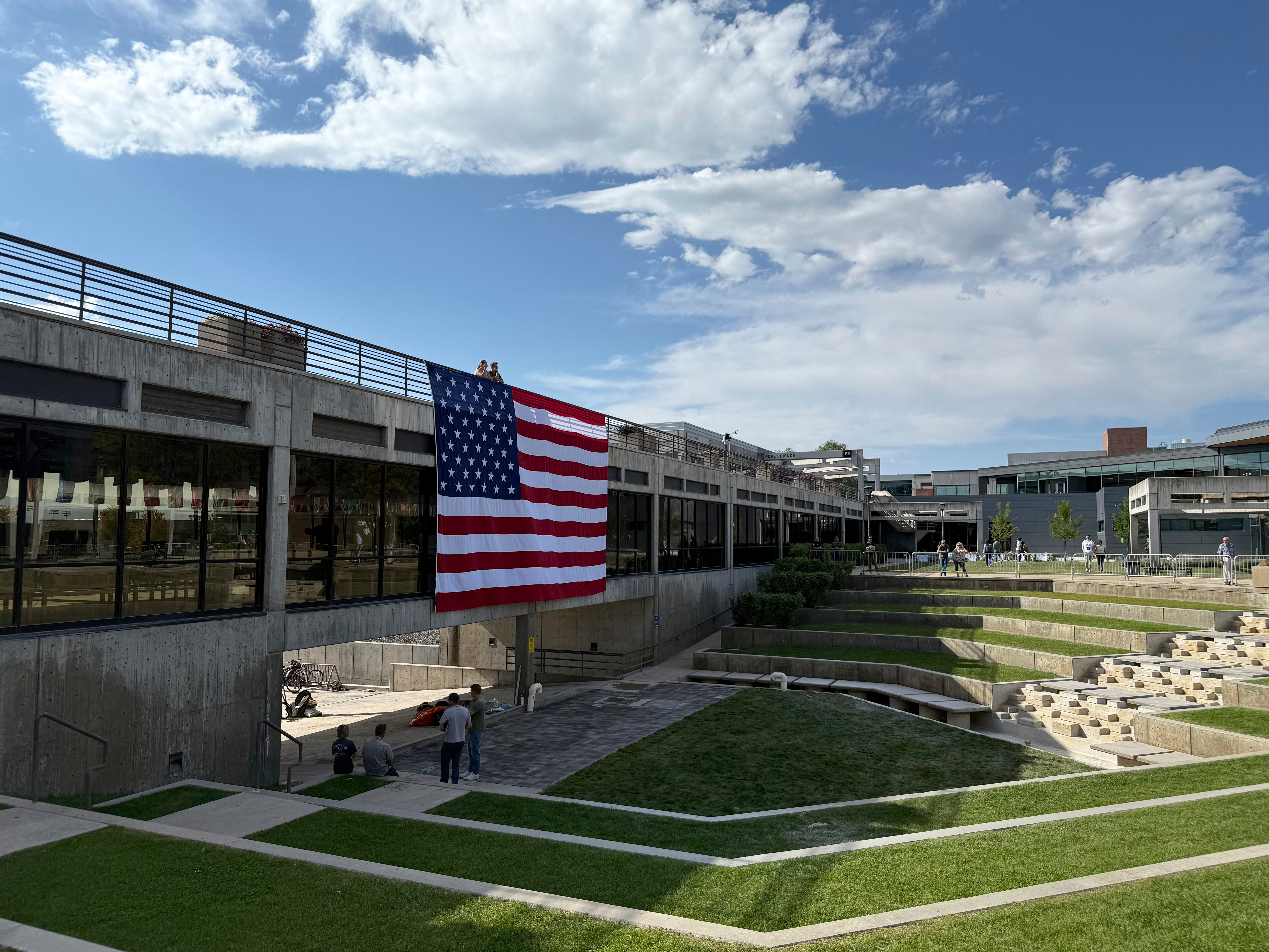 People gaze down at the site where Charlie Kirk was shot, above which hangs an American flag, at Utah Valley University on Monday, Sept. 15, 2025, in Orem, Utah. (Jesse Bedayn - AP)