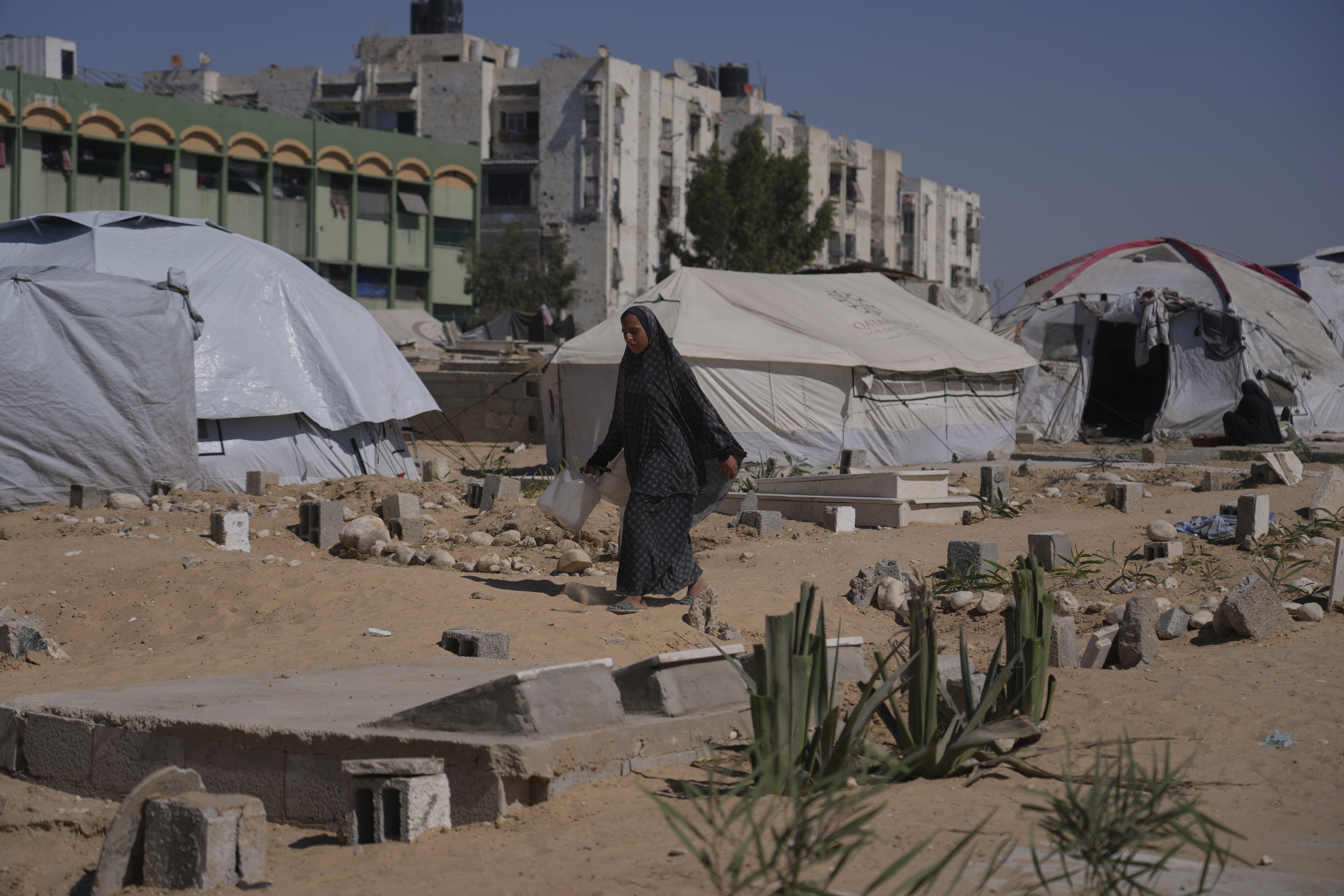 A displaced Palestinian woman walks past makeshift tents set up in a cemetery in Khan Younis, in the southern Gaza Strip, Saturday, Sept. 20, 2025. (Jehad Alshrafi - AP)