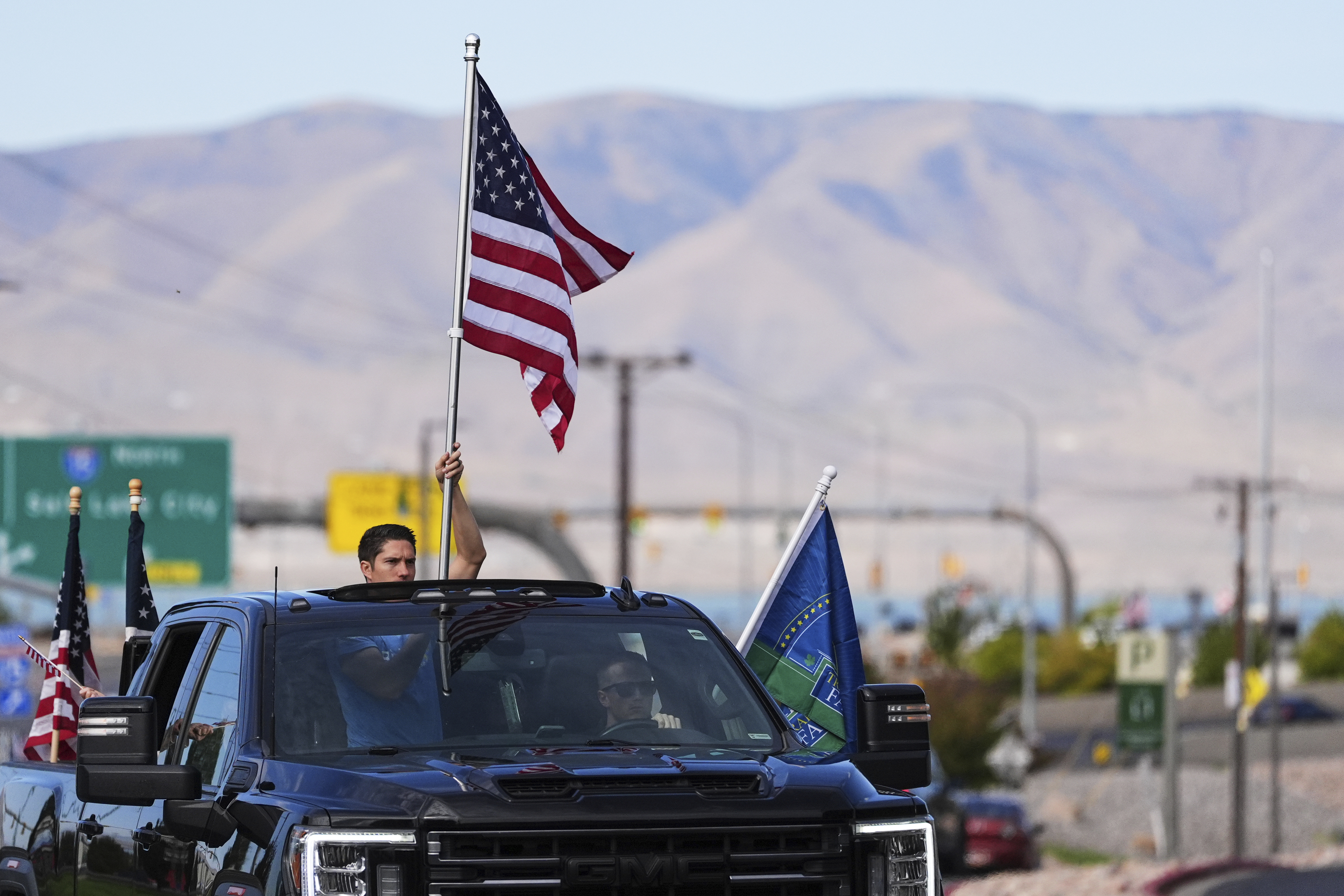A person holds an American flag out of a truck's sunroof as a brigade of vehicles drives by in tribute to Turning Point USA CEO and co-founder Charlie Kirk at Utah Valley University, Saturday, Sept. 13, 2025, in Orem, Utah. (Lindsey Wasson - AP)