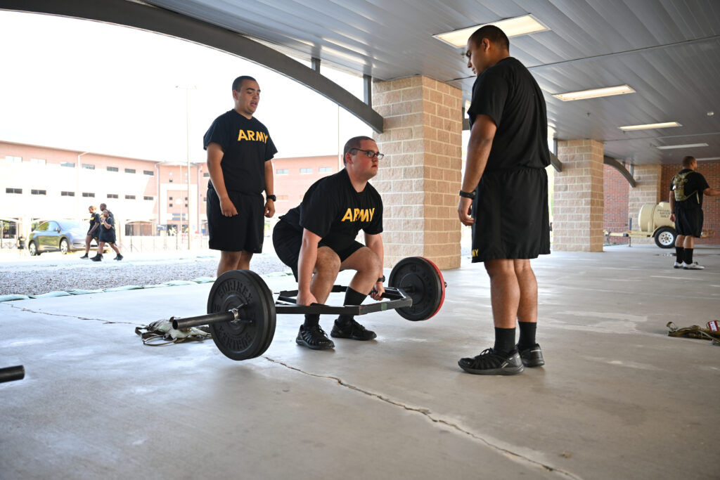 A young man in an Army shirt lifts weights from a squat.