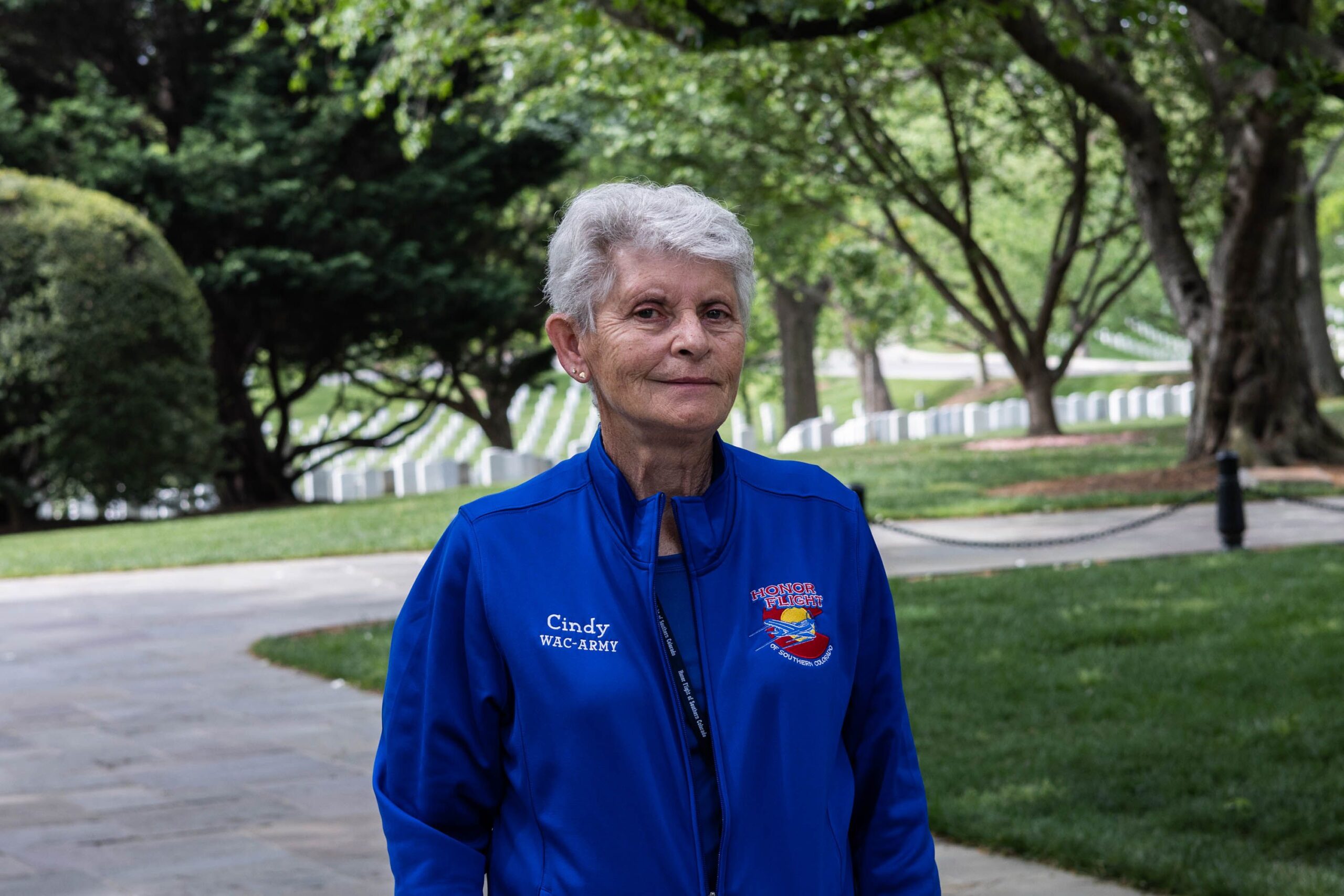 An older woman stands in a cemetery. 