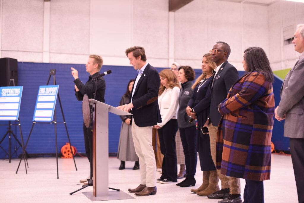 Denver Mayor Mike Johnston speaks at a podium while a sign language interpreter stands next to him