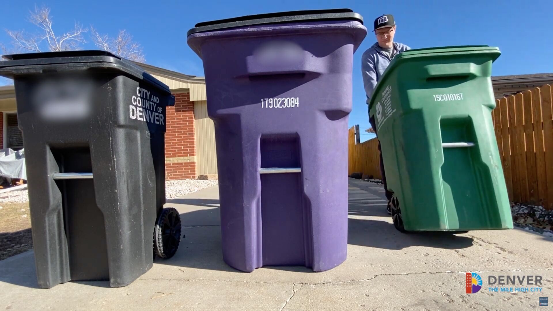 a man pushes several garbage and recycling bins to the curb