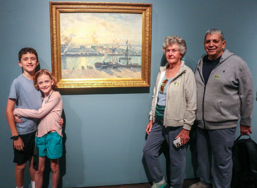 From left: Denver siblings Aila and Roan Fordham, of Denver, pose before French Impressionist painter Camille Pissarro's 'Sunset, the Port of Rouen (Steamboats)' alongside grandparents Mary McFadyen and Roderick Nasbe on Oct. 24, 2025, at the Denver Art Museum. (John Moore, Denver Gazette)