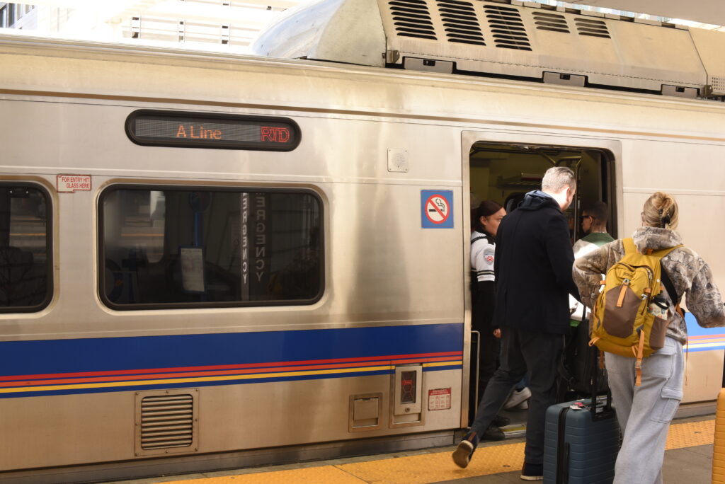 People carry backpacks and pull suitcases into a train