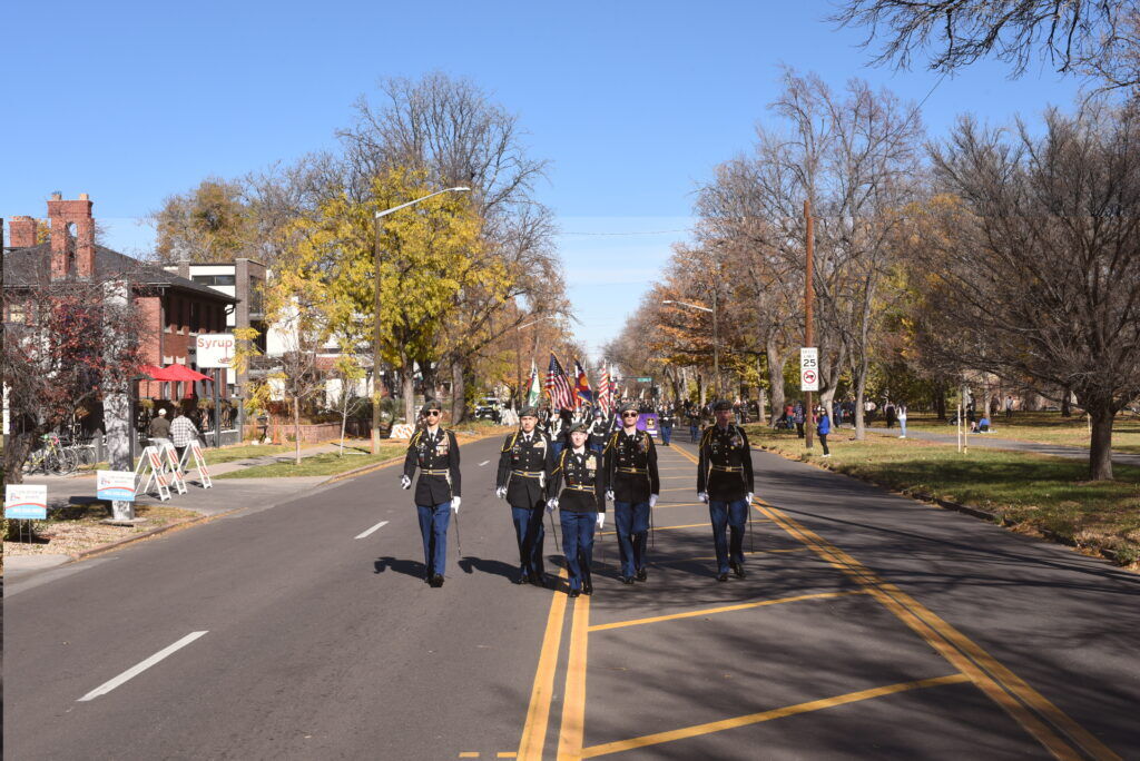Five people leading the front of a parade walking towards the camera on a roadway