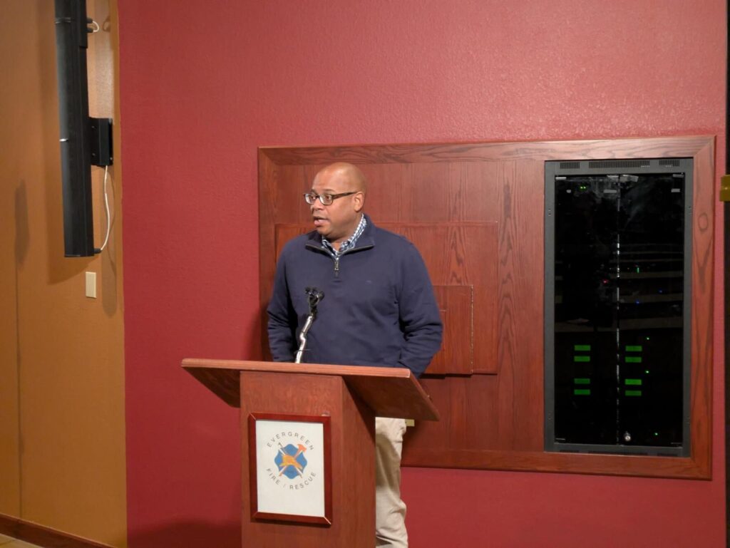 A man stands at a podium in front of a red wall