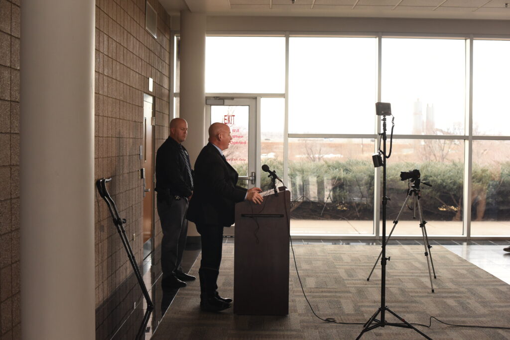 A side profile of a man standing at a podium with windows behind him
