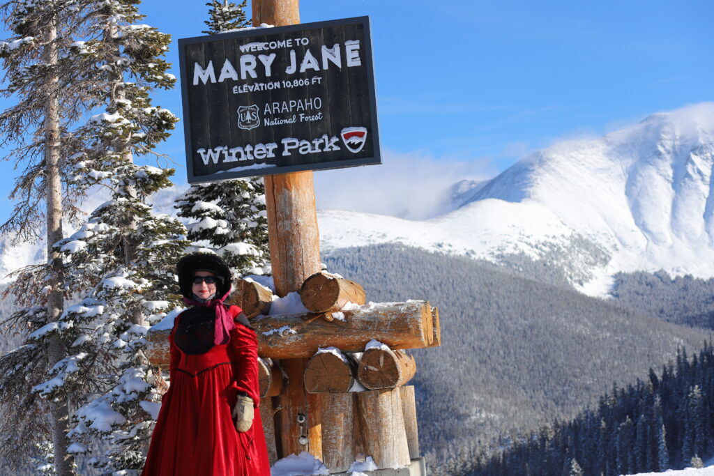 A woman stands in front of a Winter Park Resort Mary Jane sign in a red dress.