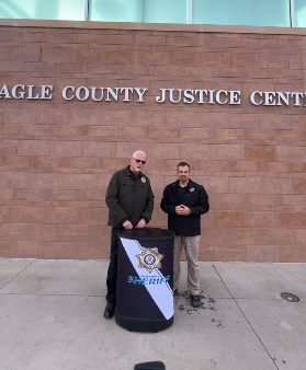 Two men speak at a podium in front of a brick background