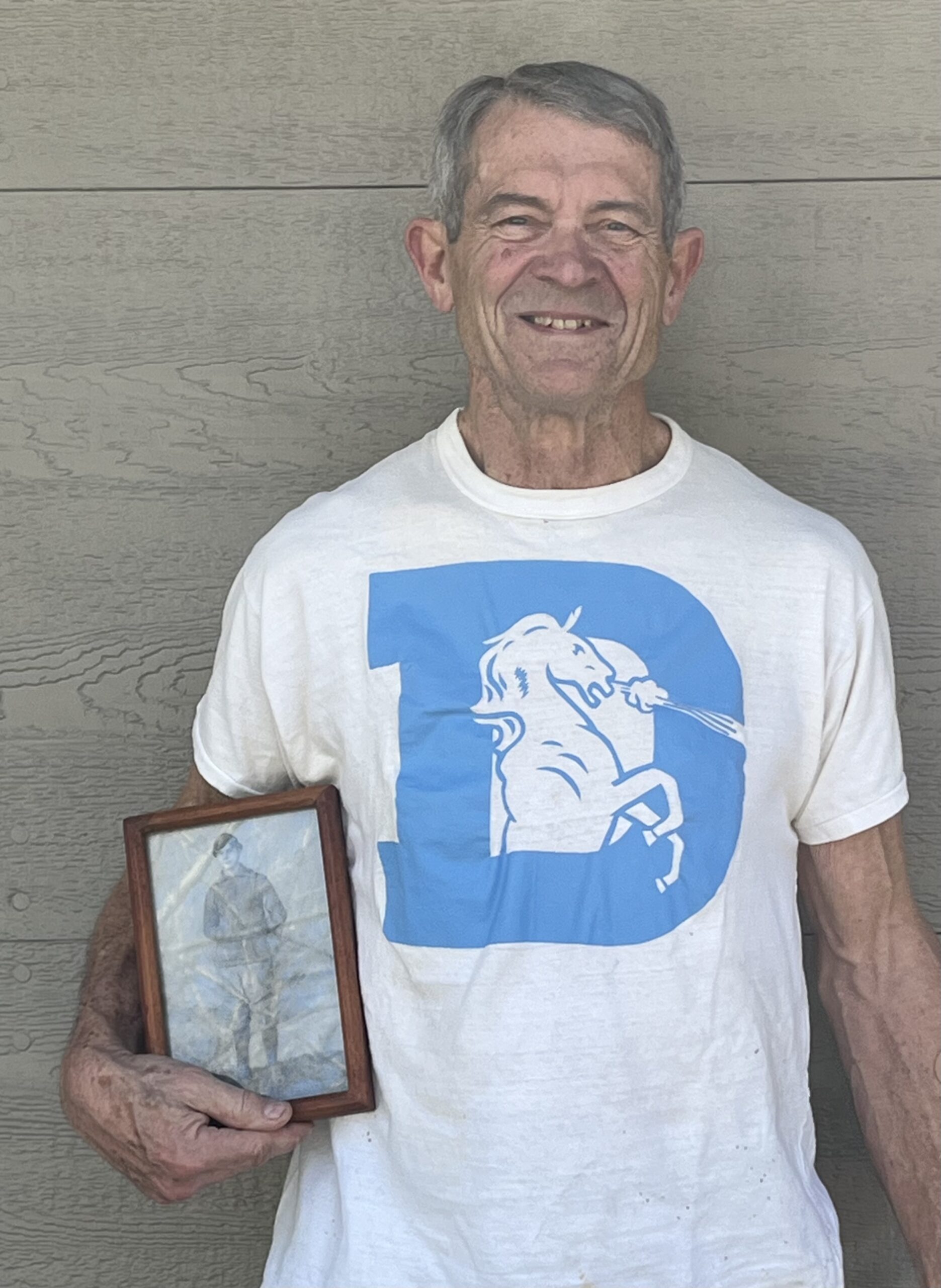Ken Shelton, a tight end who was a 15th-round pick by the Denver Broncos in 1975 out of Virginia, at his home in Hendersonville, N.C., in March 2025. Shelton elected to soon attend medical school and became a radiologist for 38 years. He is wearing a Broncos T-shirt he received from the team in 1975 while holding a photo of his great grandfather N.B. “Bull” Early, who played for Virginia in the 1890s. (Photo courtesy of Ken Shelton) (Photo courtesy of Ken Shelton)