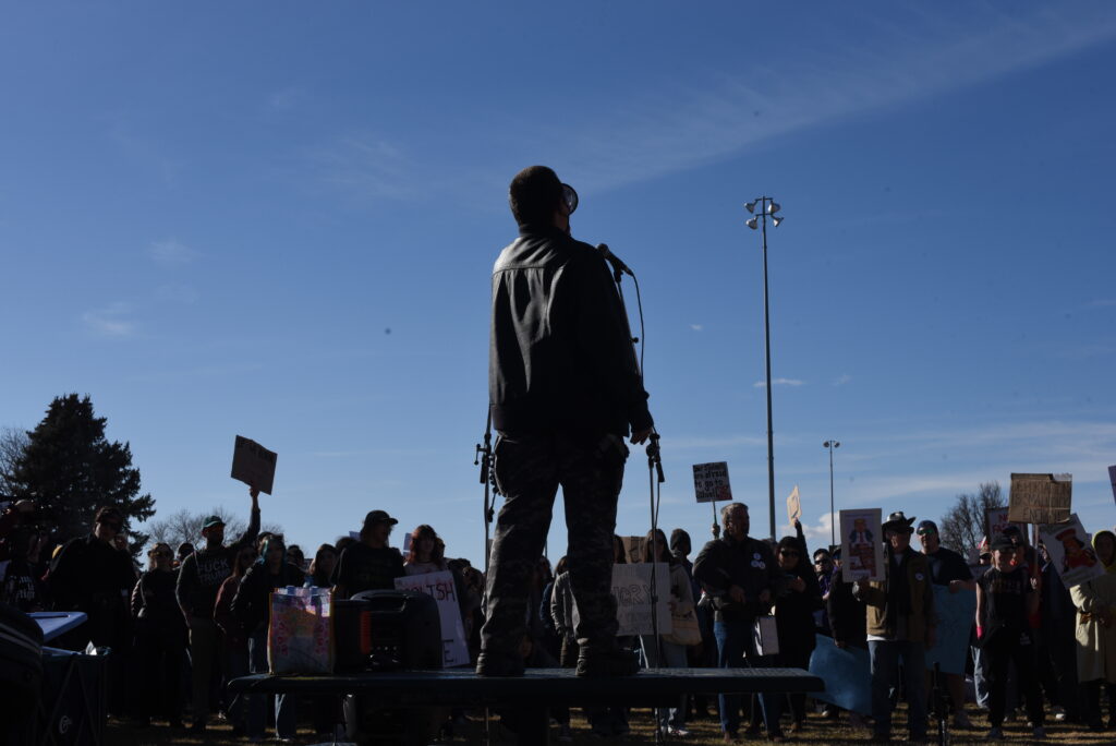 The silhouette of a person speaking into a megaphone in front of a crowd