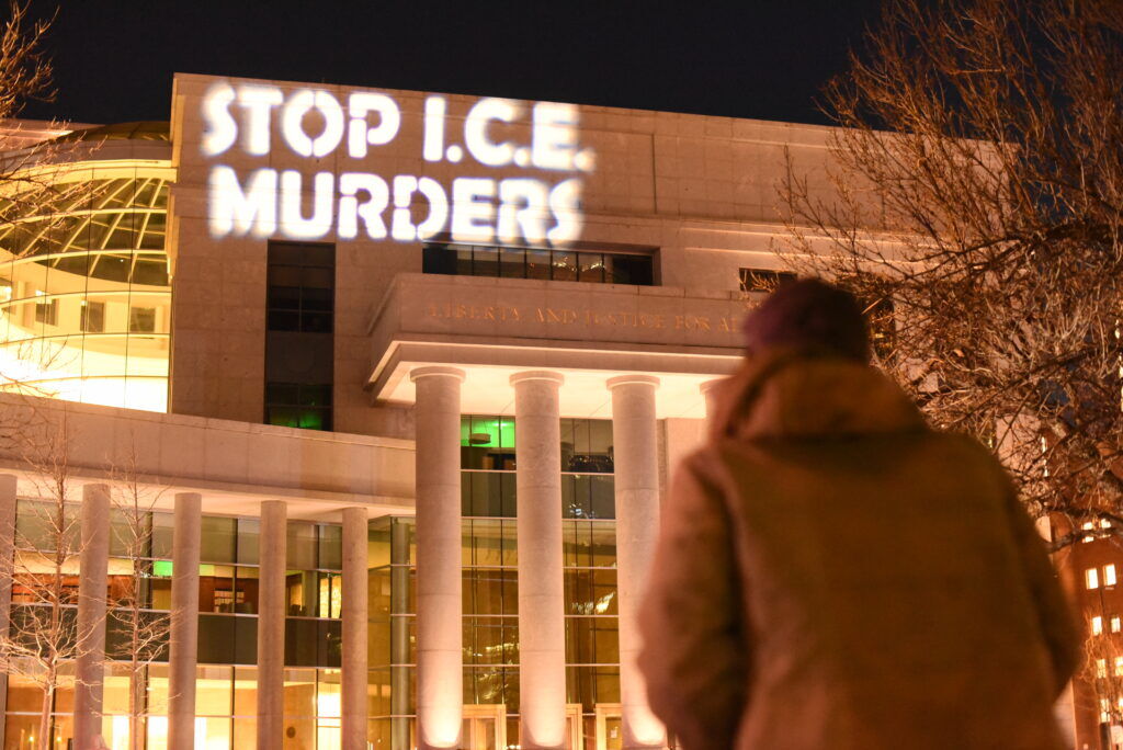 Text reading "Stop I.C.E. Murders" shines on the side of a building