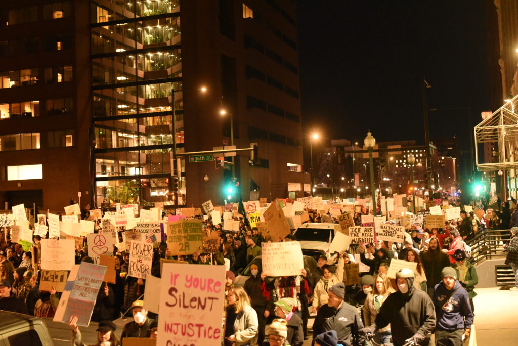 Thousands of people hold signs and walk in the middle of a street