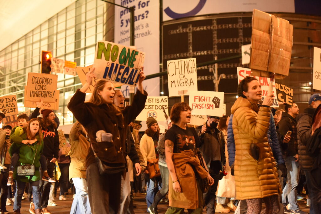 People hold signs and walk and yell in the middle of a street