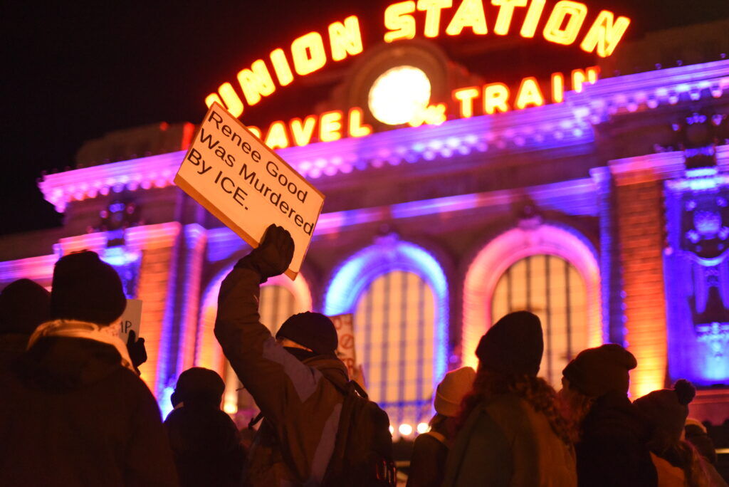 A person holds up a homemade sign with a neon sign in the background