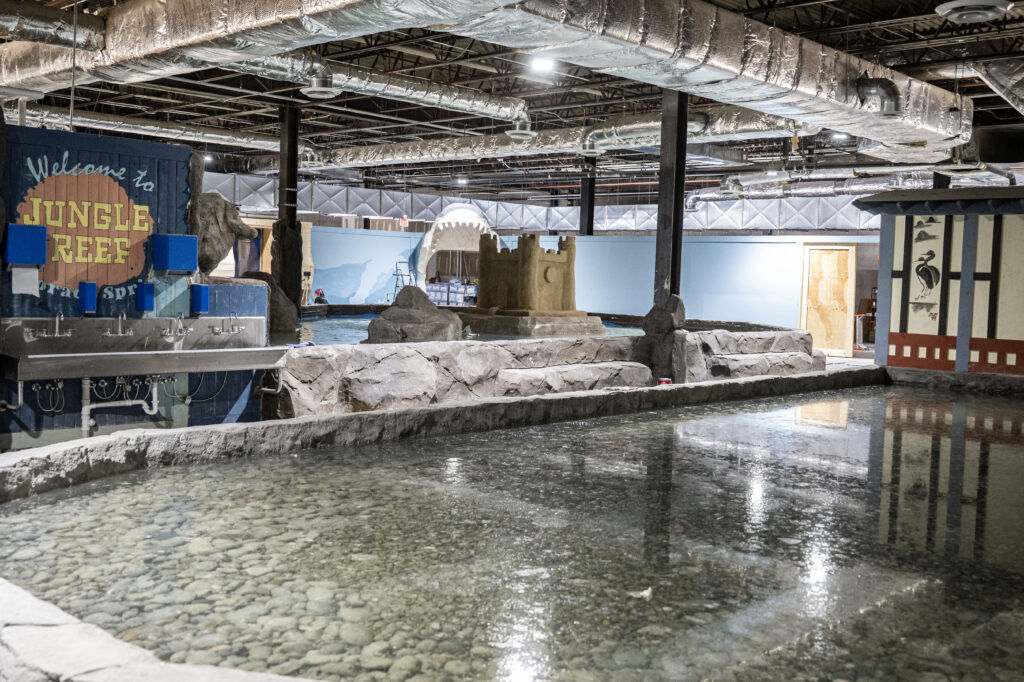 A sand castle is seen within an aquarium in Colorado springs. In the foreground is a large enclosure filled with water. 
