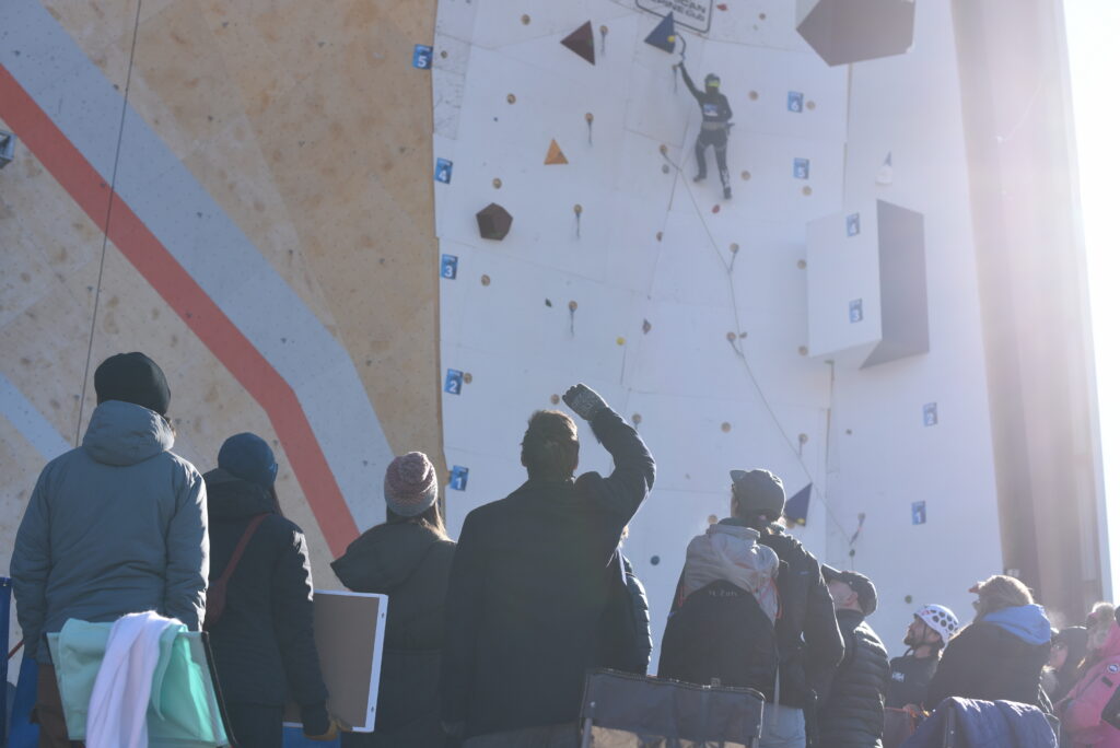 A group of people watch as a woman climbs up a wall