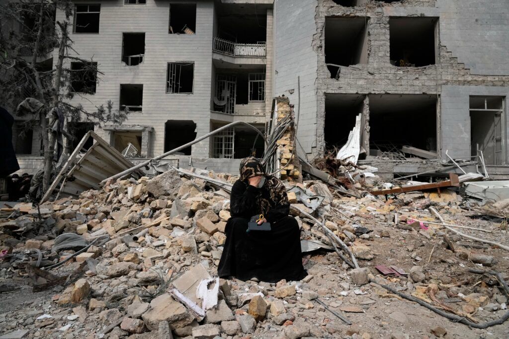 The Associated Press A woman sits on rubble across from a residential building damaged last Sunday during the U.S.-Israeli air campaign in Tehran, Iran, Thursday, March 12, 2026.