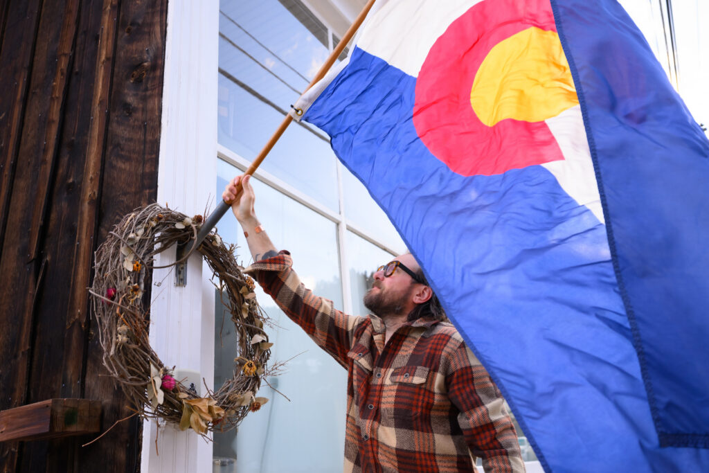 Manager Jeff Wilkins hangs a Colorado Flag outside Bread Bar in Silver Plume, Colorado Friday, January 30, 2026. Bread is a small cocktail bar in a former 1800’s bakery in the historic mountain town west of Denver on I-70. Photo by Mark Reis