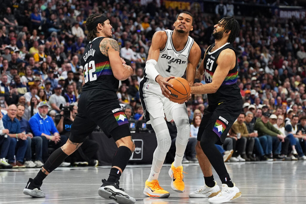San Antonio Spurs center Victor Wembanyama is fouled by Denver Nuggets guard Jamal Murray, right, while driving past forward Aaron Gordon in the first half of an NBA basketball game, Saturday, April 4, 2026, in Denver. (AP Photo/David Zalubowski)
