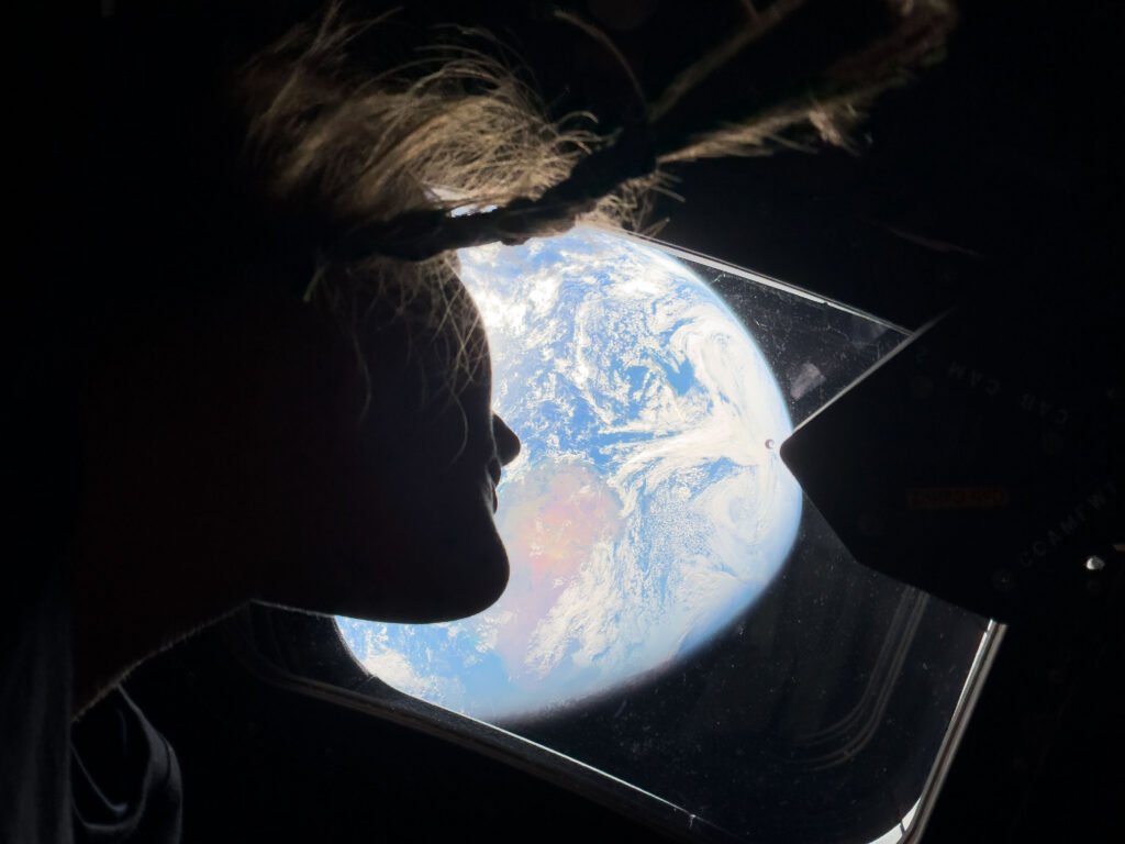 An astronaut looks out the window of her spacecraft as it orbits earth.
