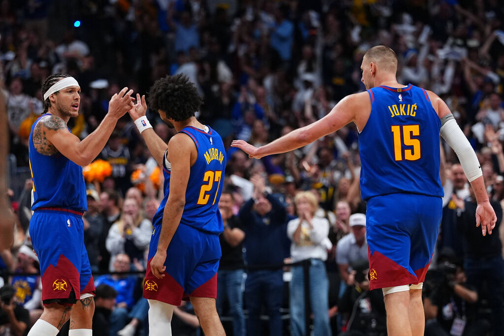 Denver Nuggets guard Jamal Murray (27) is congratulated by teammates Aaron Gordon, left, and Nikola Jokic (15) after hitting a 3-point basket at the buzzer to end the first half against the Minnesota Timberwolves in Game 2 of a first-round NBA playoffs basketball series Monday, April 20, 2026, in Denver. (AP Photo/Jack Dempsey)
