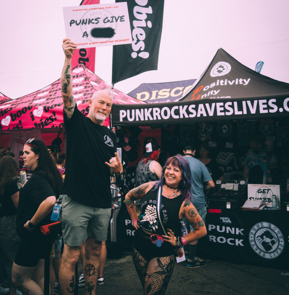 OK, yes, we blurred the sign that Punk Rock Saves Lives founder Rob Rushing held up in front of his nonprofit's festival booth. You can probably figure it out. He's shown with his wife, co-founder Tina Rushing. (Courtesy Punk Rock Saves Lives)