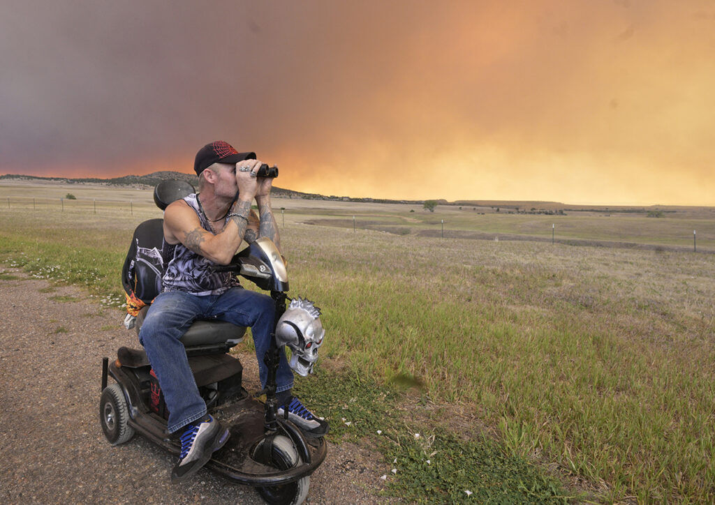 Justin Burk looks through the binoculars from a road near his home in Mountain Shadows Mobile Estates, keeping an eye on the Aspen Acres Fire.