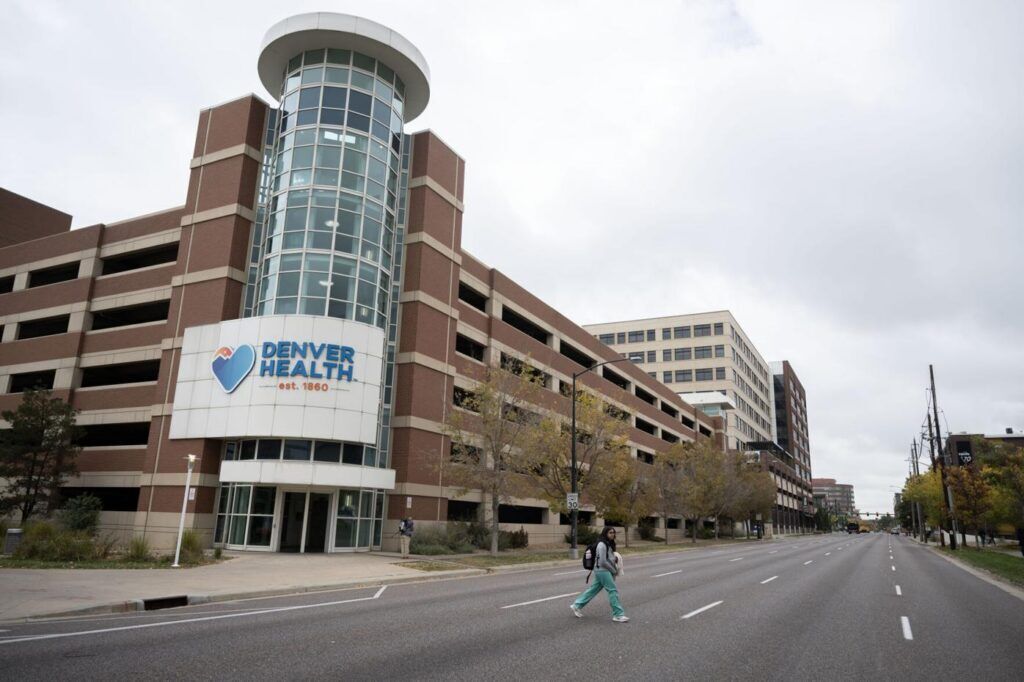 a medical worker crosses a street in front of a major metro hospital building