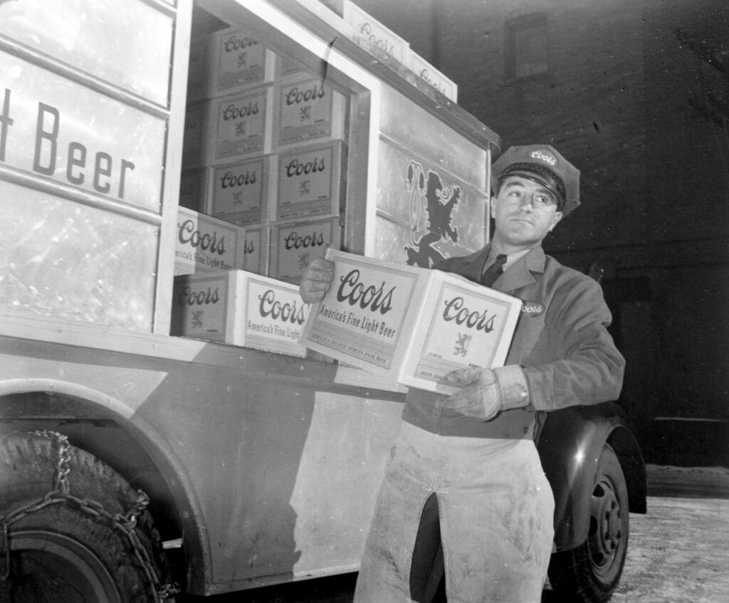 a historic photo of a Coors delivery driver unloading cases of beer