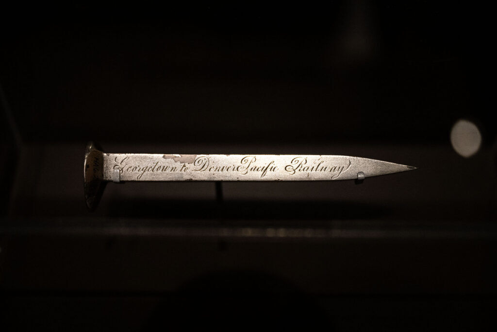 a decorative railroad spike behind a glass case at History Colorado