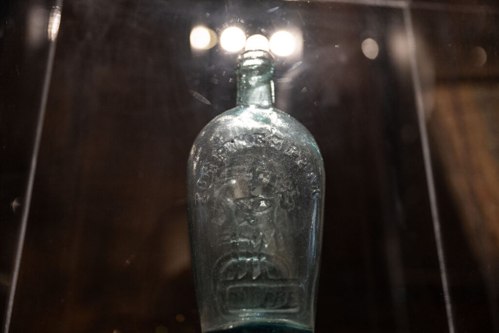 A glass whiskey bottle with "Pikes Peak" written on it behind a glass case at History Colorado.
