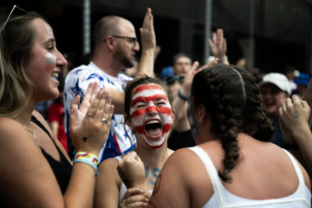 Fans with painted faces celebrate with one another as USA scores a goal.