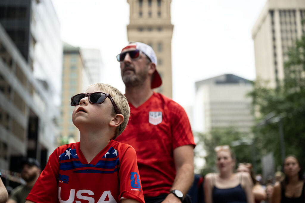 Eddie Kelly, 7, and his dad Jim sit on the turf at Skyline Park during a watch party for the USA vs Bosnia-Herzegovina game on Wednesday, July 1, 2026.