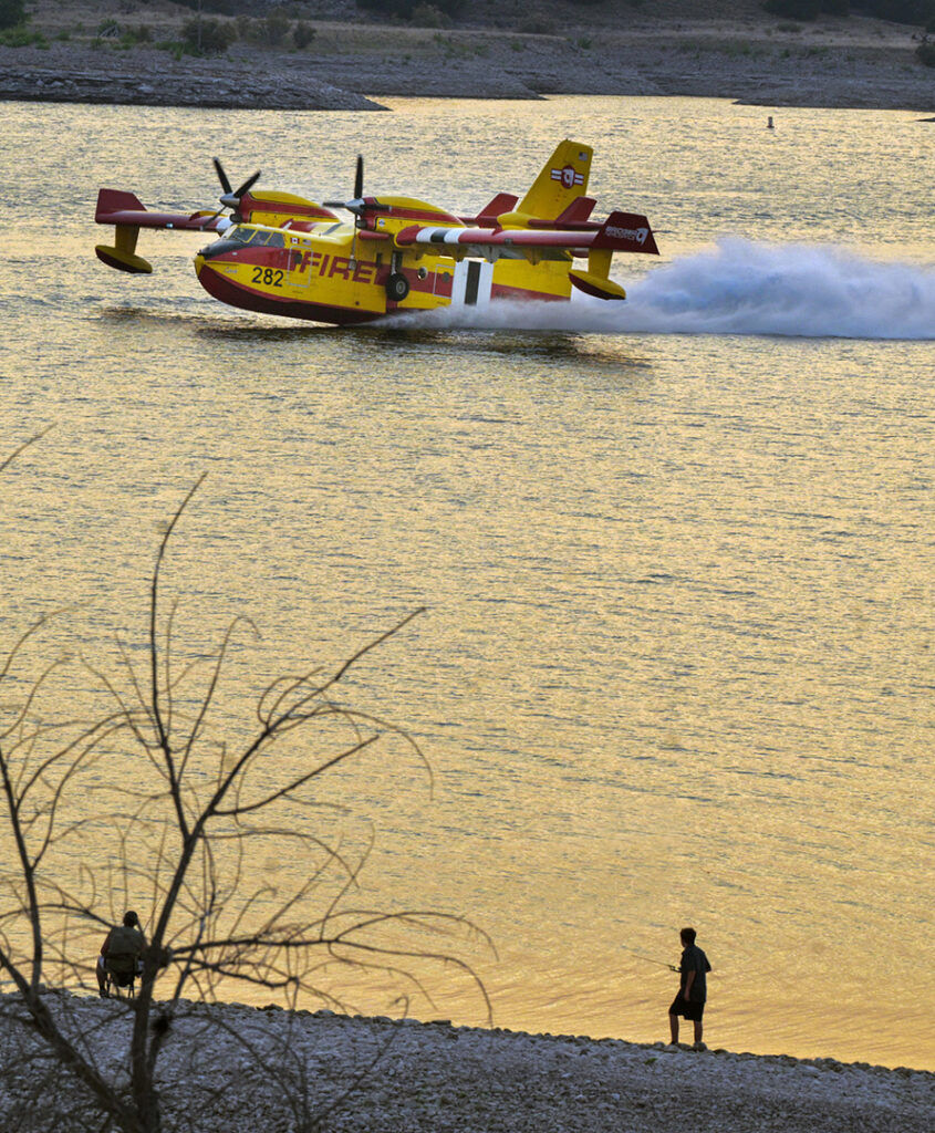Fishermen watch at dusk as a Bridger Aerospace Tanker skims along the surface of the Pueblo Reservoir to scoop up water to drop on the northern face of the Aspen Acres Fire on Sunday, July 5, 2026. (The Gazette, Jerilee Bennett)