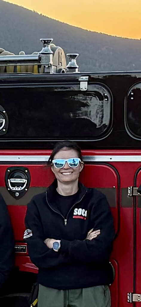 Volunteers with the Southern Colorado Interagency Fire Team, including Amanda Wood, and firefighters from Fort Carson work on "prep and hold" structure protection during the Aspen Acres fire, July 1. Wood is pictured here posing in front of a fire engine, during a previous call-out. Photo courtesy of Amanda Wood.
