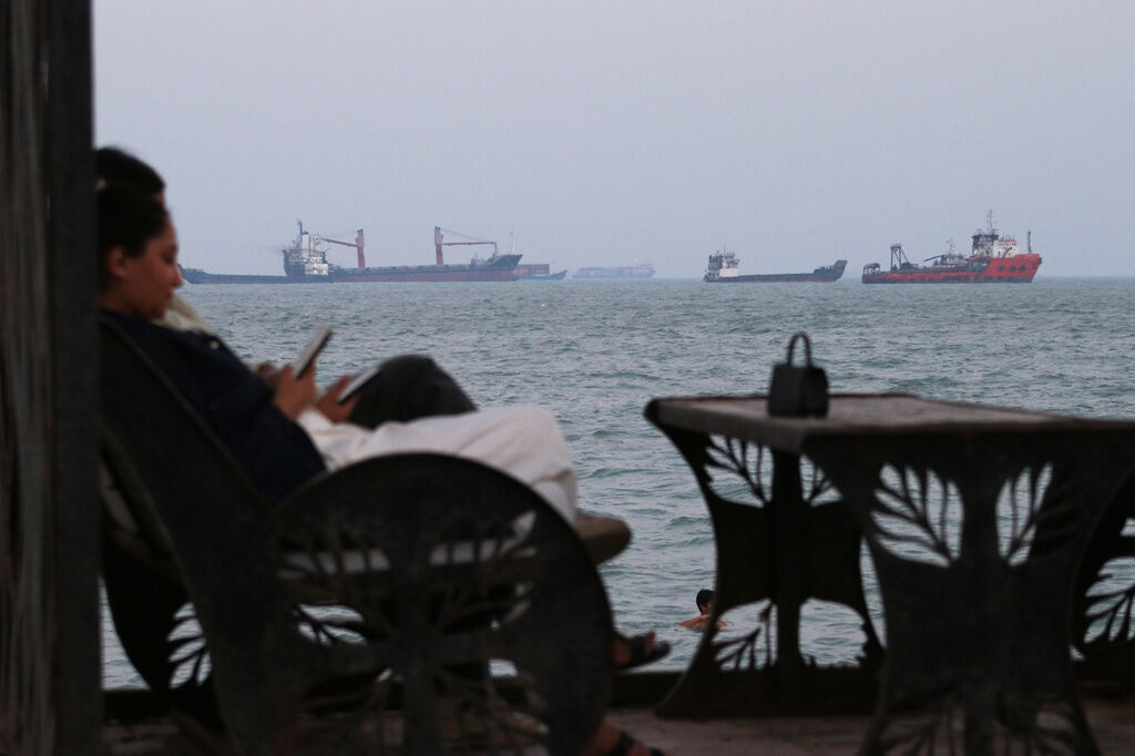 Residents check their cellphones as they sit at a cafe overlooking commercial vessels anchored in the Strait of Hormuz, off Bandar Abbas, Iran, Sunday, July 12, 2026. (Razieh Poudat/ISNA via AP)