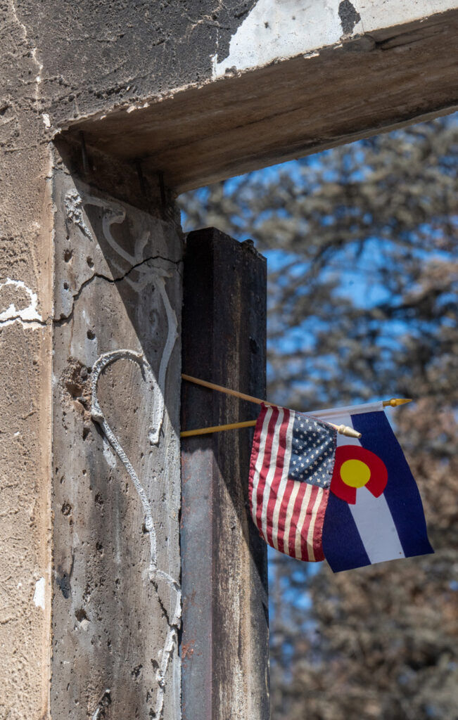 A Colorado and U.S. flag hang in the doorway of a demolished home off on Pine Dr. in Beulah after the Aspen Acres Fire on Tuesday, July 14, 2026. (The Gazette/ Jerilee Bennett)