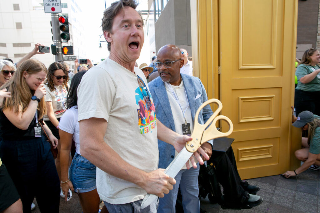 A man holds a pair of giant scissors in front of a crowd