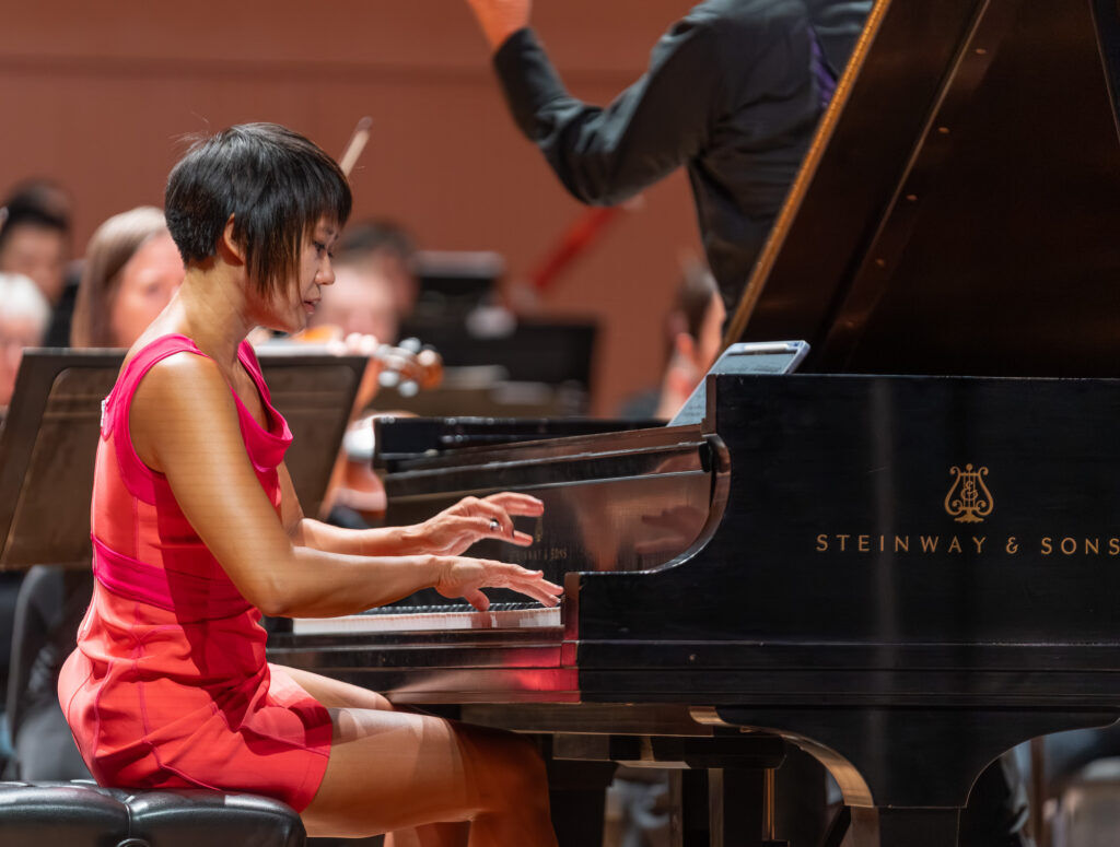 Pianist Yuja Wang in a bright pink dress playing the piano in Boulder