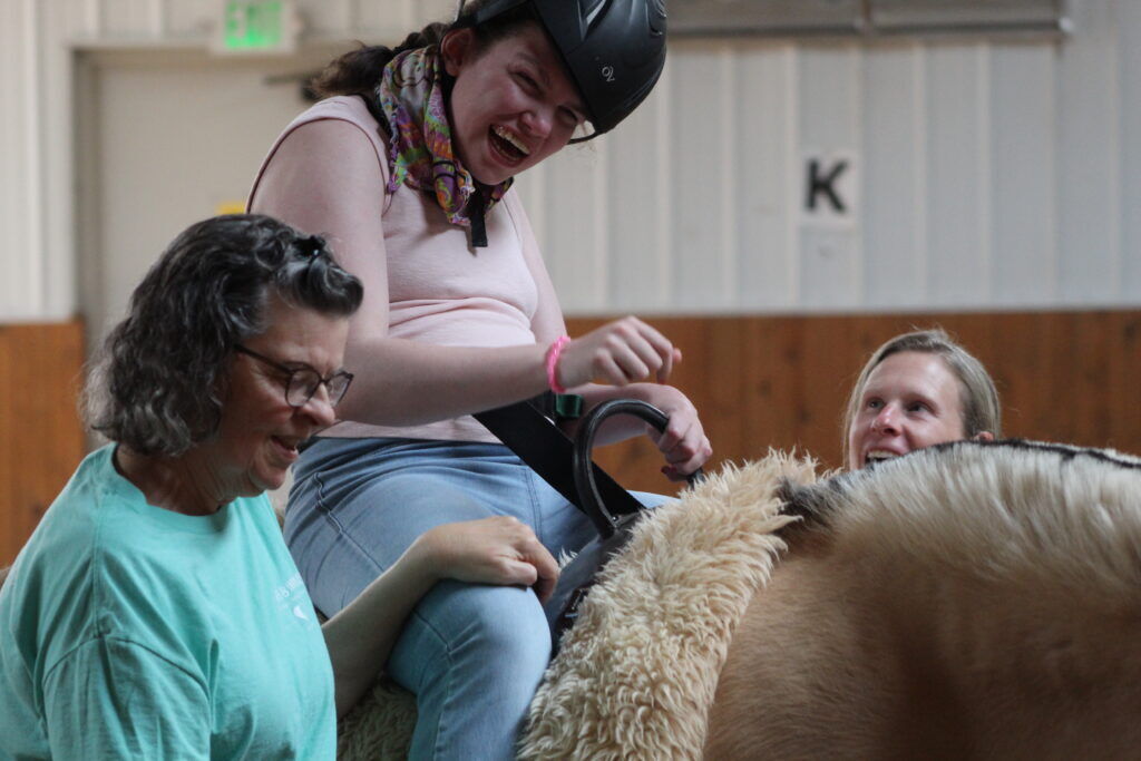 Tegan Motschall smiles while sitting on a therapy horse as two women assist her at Hearts & Horses Therapeutic Riding Center in Loveland.