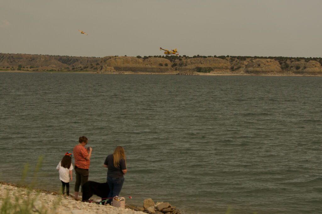 Visitors at Lake Pueblo State Park watch as a pair of Super Scoopers depart after filling their water tanks. The scoopers are working with a team of more than 600 firefighters to combat the Aspen Acres fire, which grew to over 85,000 acres as of Saturday, July 4, 2026. The fire is, as of a morning update Saturday, uncontained. (Mary Shinn, The Gazette)