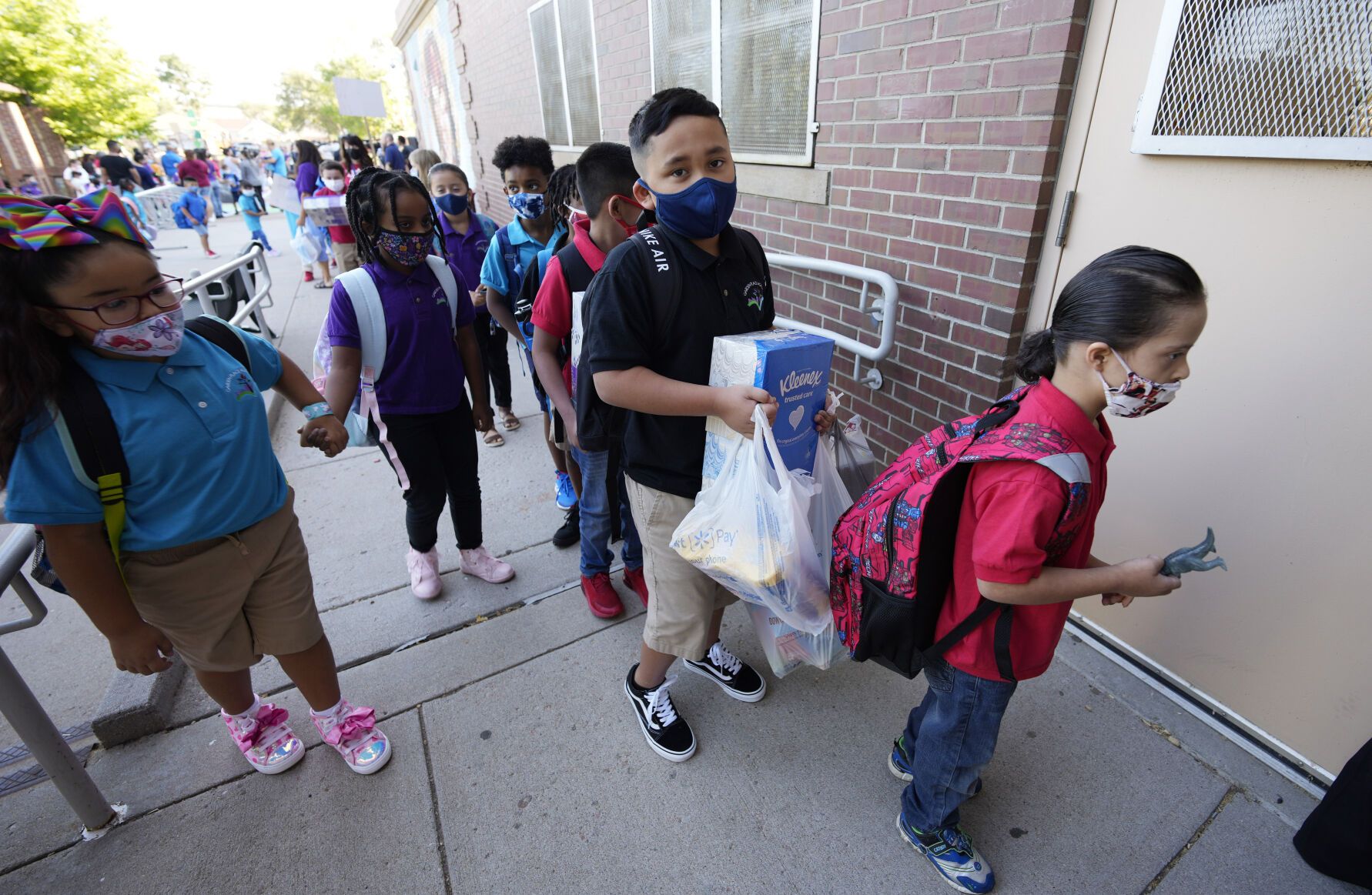 A child carries boxes of facial tissues and a bag of other cleaning supplies as he joins classmates in heading in for the first day of in-class learning since the start of the pandemic at Garden Place Elementary School Monday, Aug. 23, 2021, in north Denver (AP Photo/David Zalubowski)