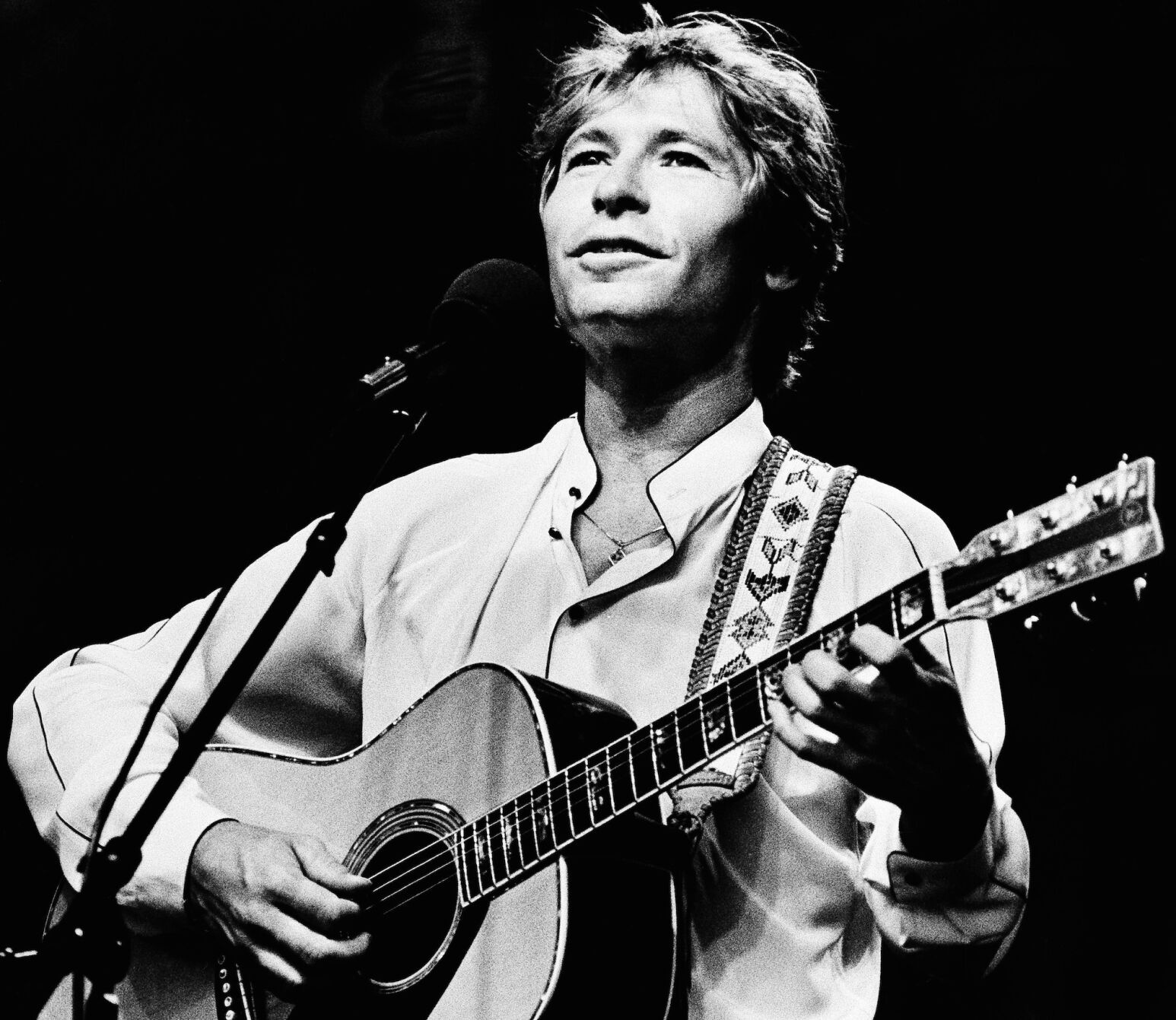 Singer John Denver strums his guitar as he performs during an outdoor concert on the Boston Common in Boston, Mass., on July 28, 1983.
